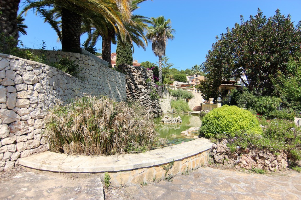 Jardín mediterráneo con estanque ornamental, cascada de piedra natural y muros de mampostería rodeados de palmeras y vegetación autóctona.