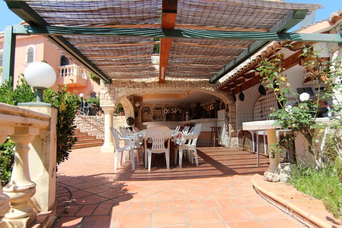 Terraza cubierta con arcos de piedra natural, zona de comedor para grupos grandes y cocina exterior integrada bajo un techo de cañizo.