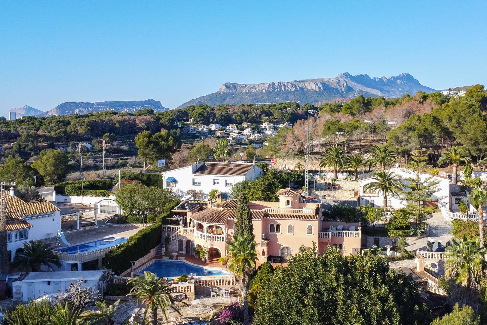 Vista aérea de la villa de estilo mediterráneo con piscina privada y amplias terrazas, integrada en un entorno natural con vistas a las montañas.