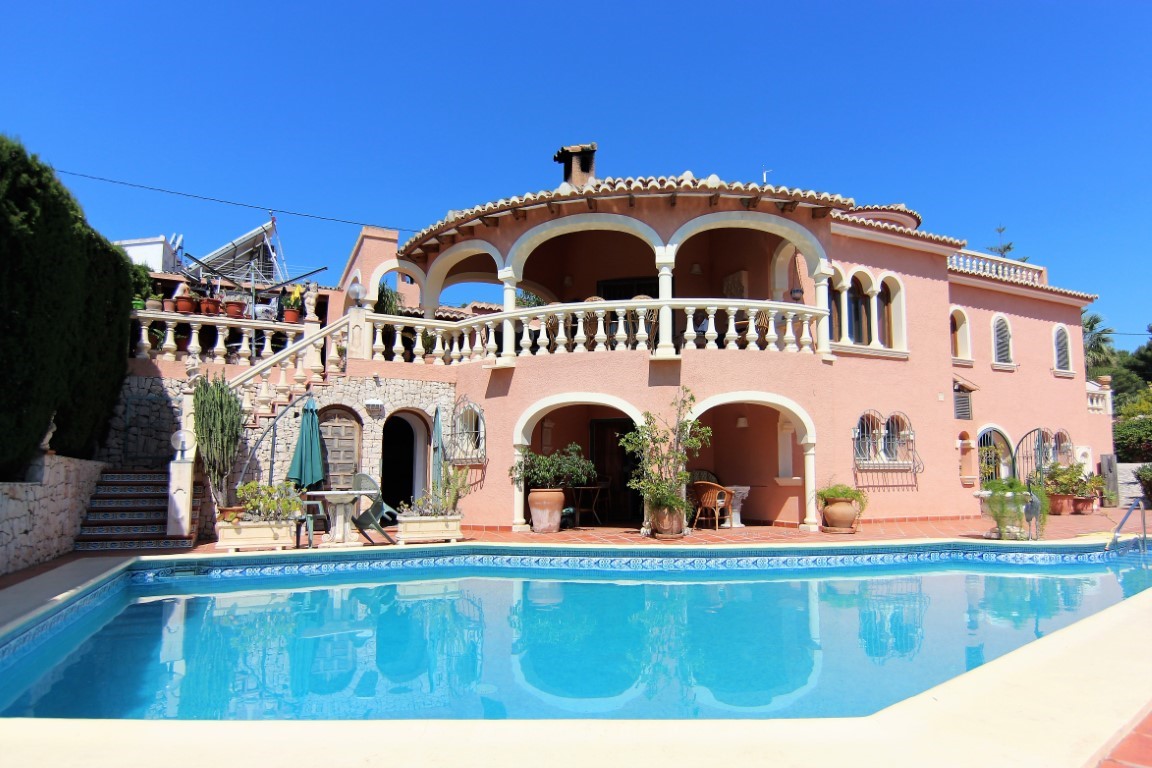 Vista exterior de la villa con piscina rectangular, destacando las terrazas arqueadas en dos niveles y la fachada de estilo mediterráneo en tonos terracota.