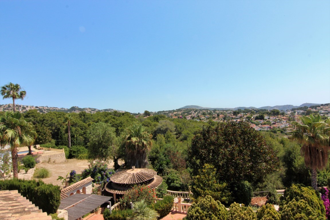 Vista panorámica desde la terraza superior que muestra el jardín mediterráneo con palmeras, un cenador circular con tejado de tejas y colinas residenciales al fondo.