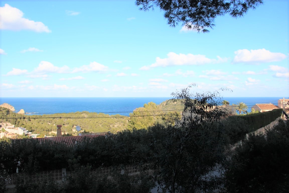 Vista panorámica al mar Mediterráneo desde la parcela, rodeada de vegetación autóctona y tejados tradicionales en un entorno residencial tranquilo.