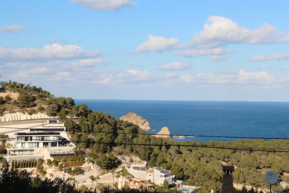 Vista panorámica desde la parcela hacia el mar Mediterráneo y la isla del Portichol, con villas modernas integradas en la ladera arbolada de Jávea.