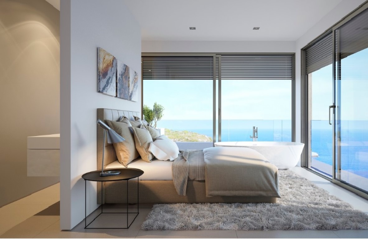 Dormitorio principal con bañera exenta junto a grandes ventanales, ofreciendo vistas panorámicas al mar y acceso directo a la terraza.