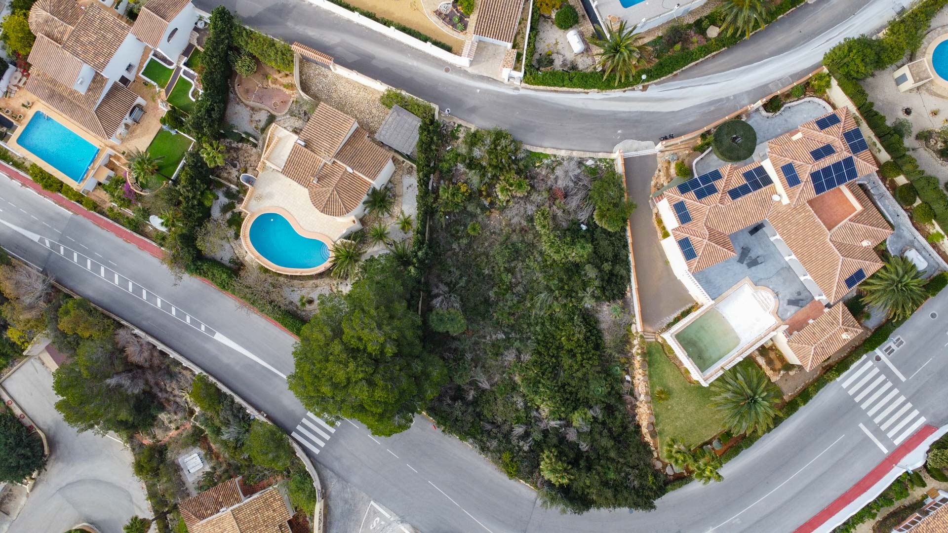 Vista aérea cenital que muestra la distribución de las parcelas, las cubiertas de teja mediterránea, piscinas privadas y la integración de paneles solares en la zona.