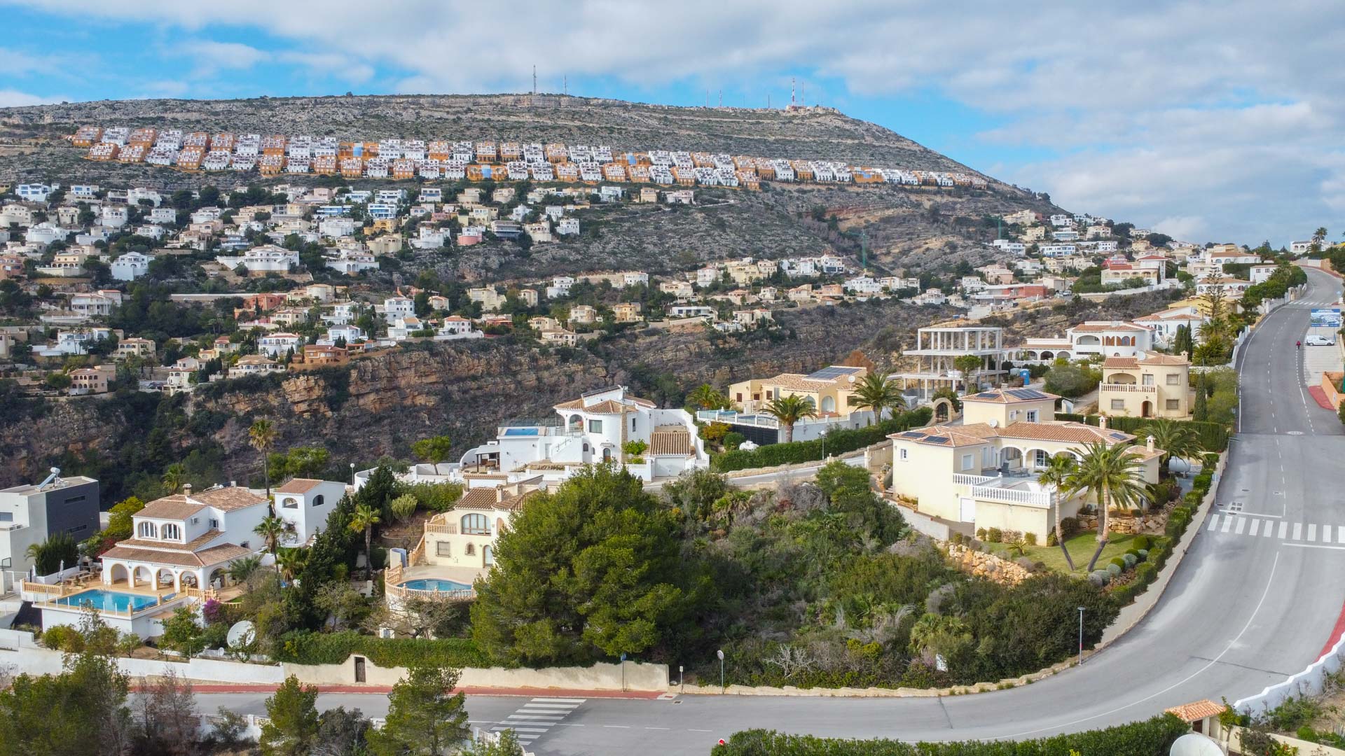 Vista aérea panorámica de la urbanización Cumbre del Sol, destacando la disposición de las villas en la ladera y el entorno natural mediterráneo.