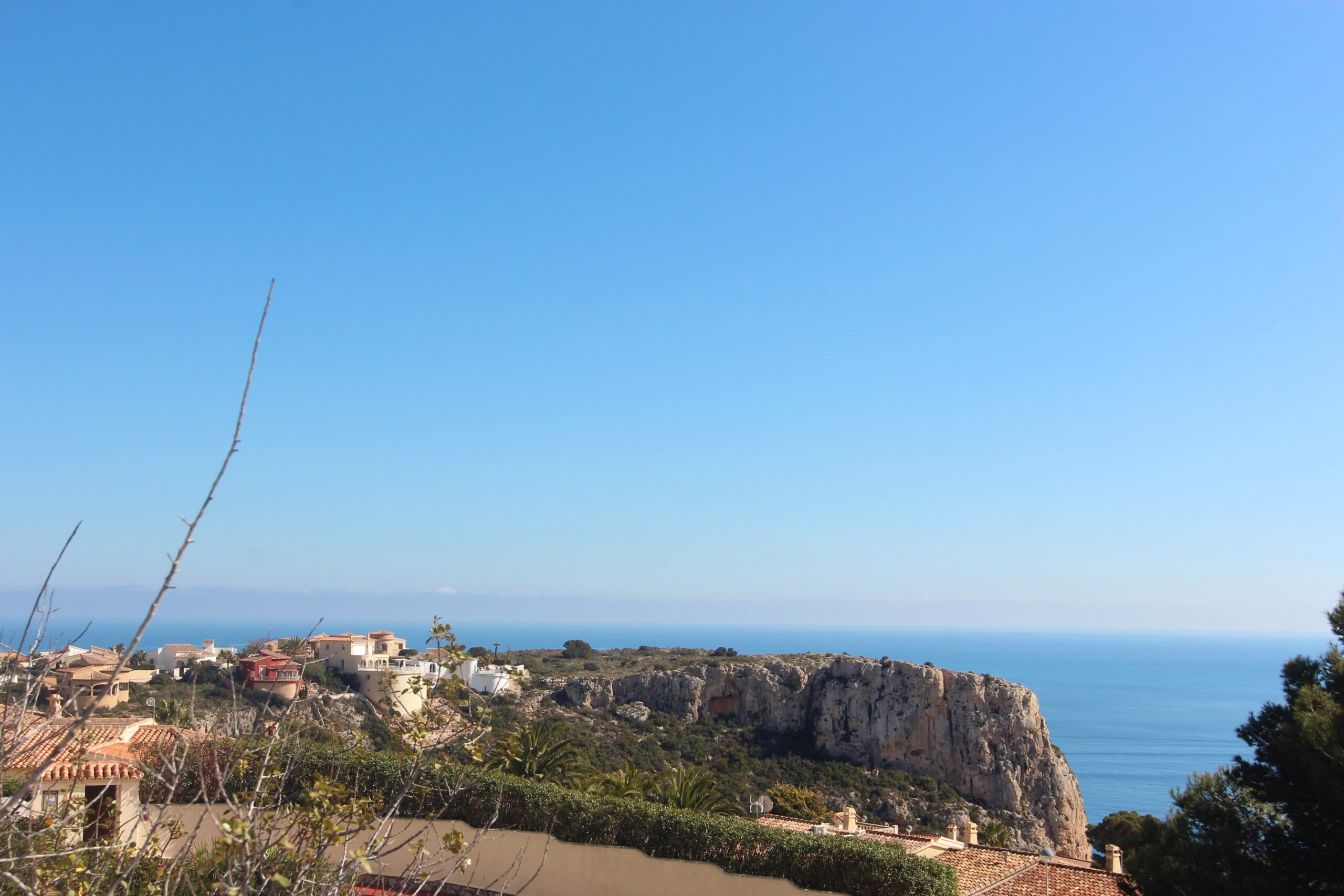 Vista panorámica desde la propiedad hacia el mar Mediterráneo y los acantilados de Cumbre del Sol, con tejados tradicionales y vegetación autóctona bajo un cielo despejado.