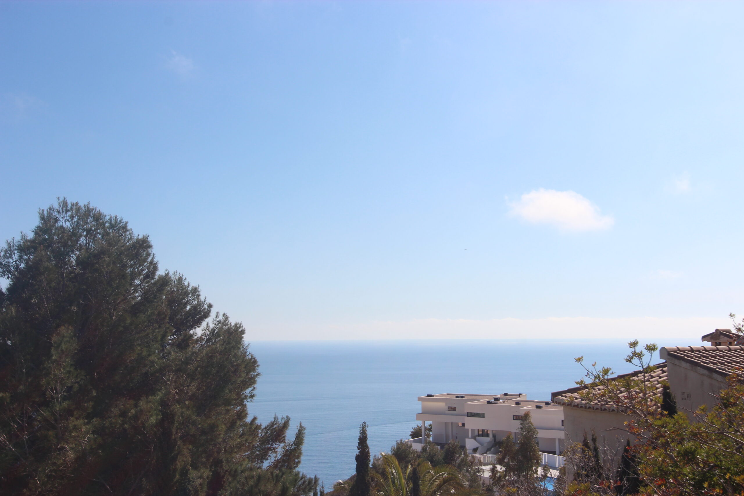 Vistas panorámicas al mar Mediterráneo desde una posición elevada, rodeada de pinos maduros y arquitectura moderna en la zona de Cumbre del Sol.