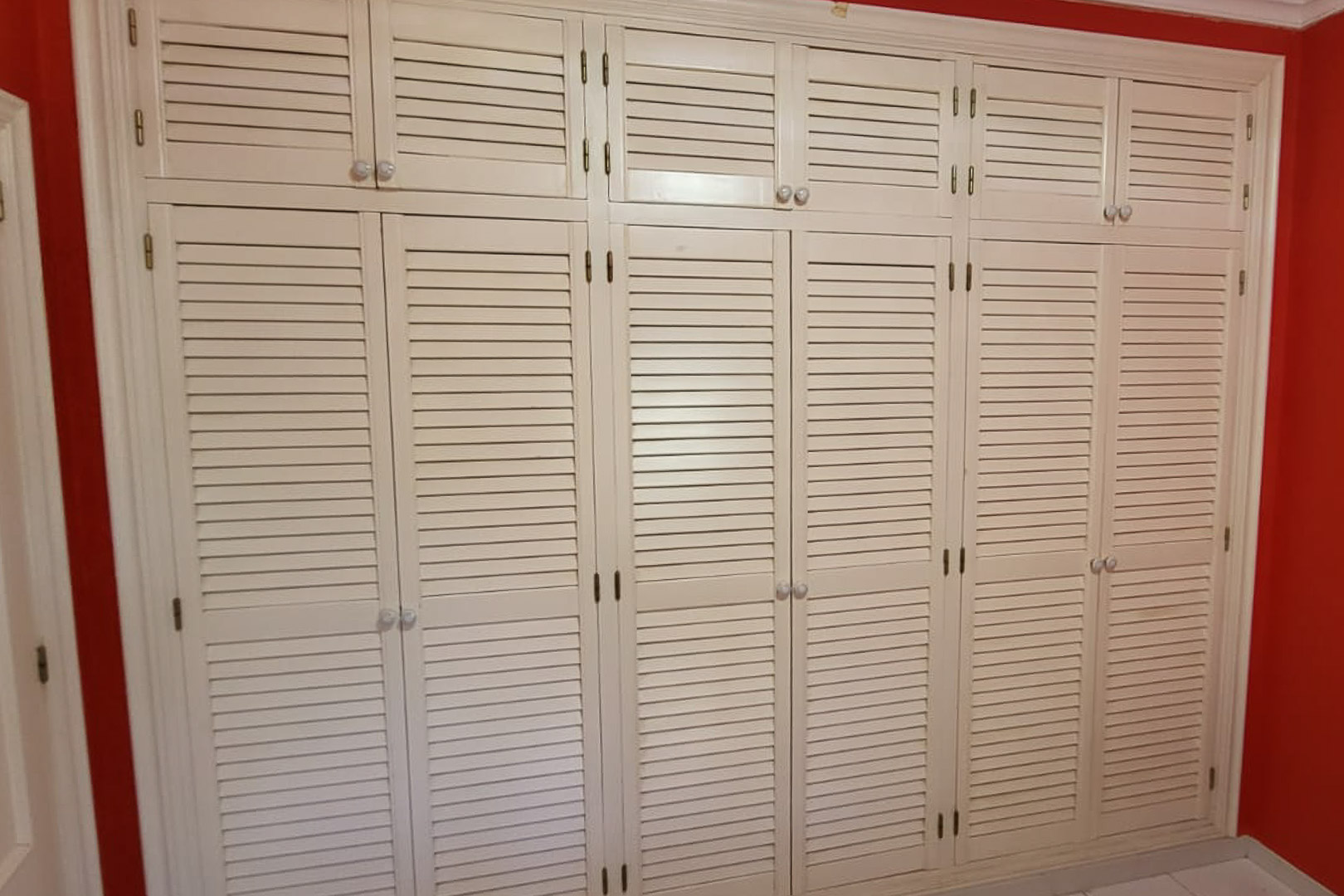 Armario empotrado con puertas de persiana en dormitorio con pared roja.