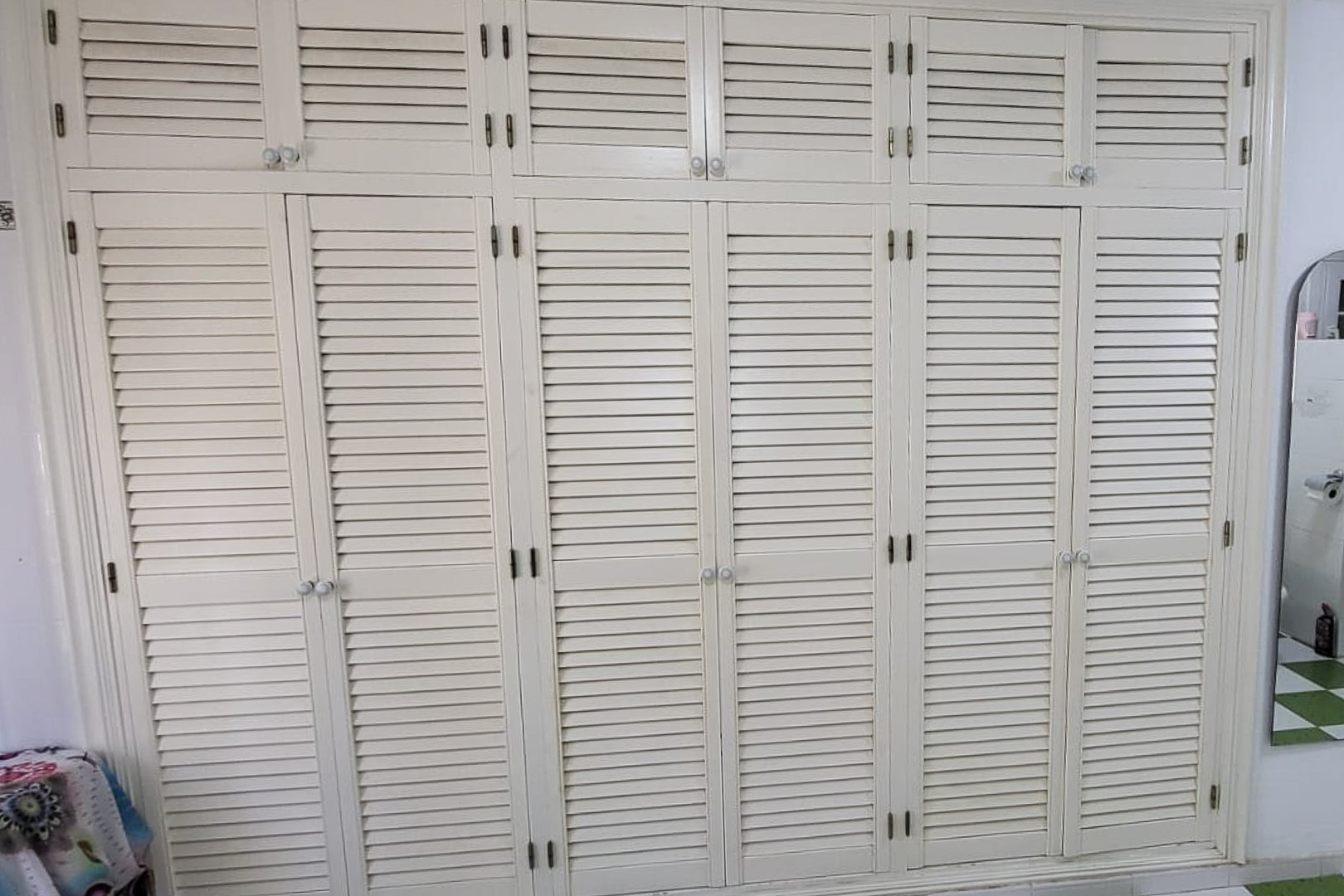 Armario empotrado de madera con puertas de persiana y pomos redondos, que ocupa toda la pared.