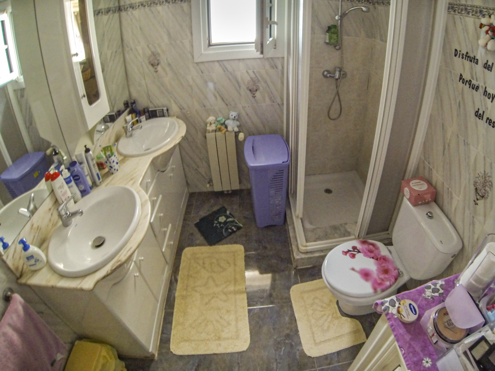 Cuarto de baño con dos lavabos, ducha con mampara y WC con tapa decorada.