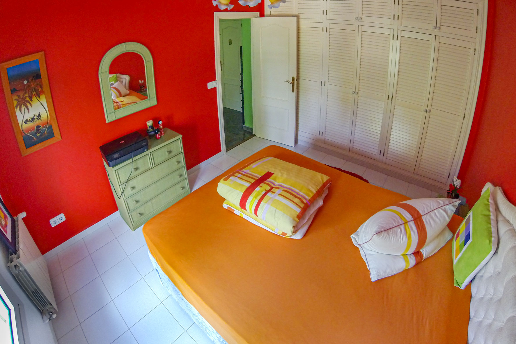 Dormitorio con paredes rojas, armario empotrado blanco y cama con ropa de cama naranja.