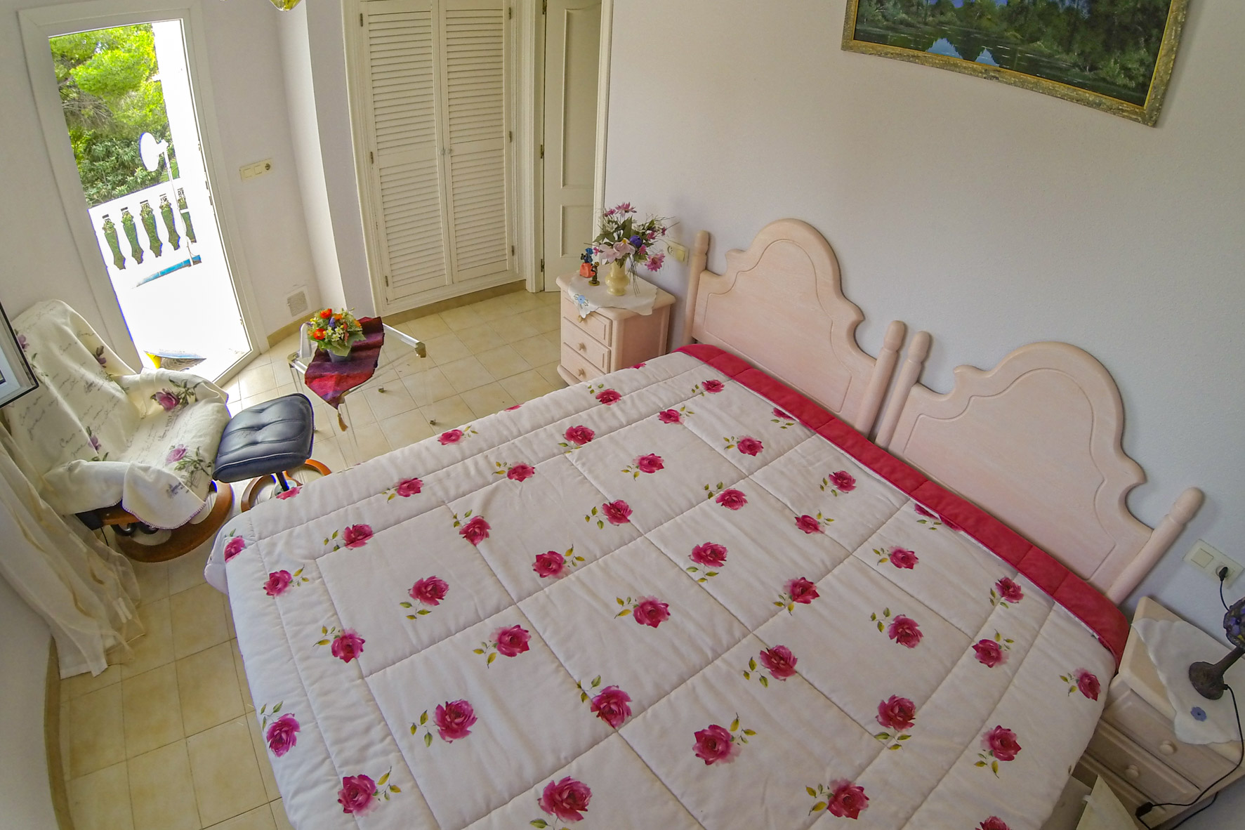 Dormitorio luminoso con cama doble, ropa de cama floral y acceso a la terraza.