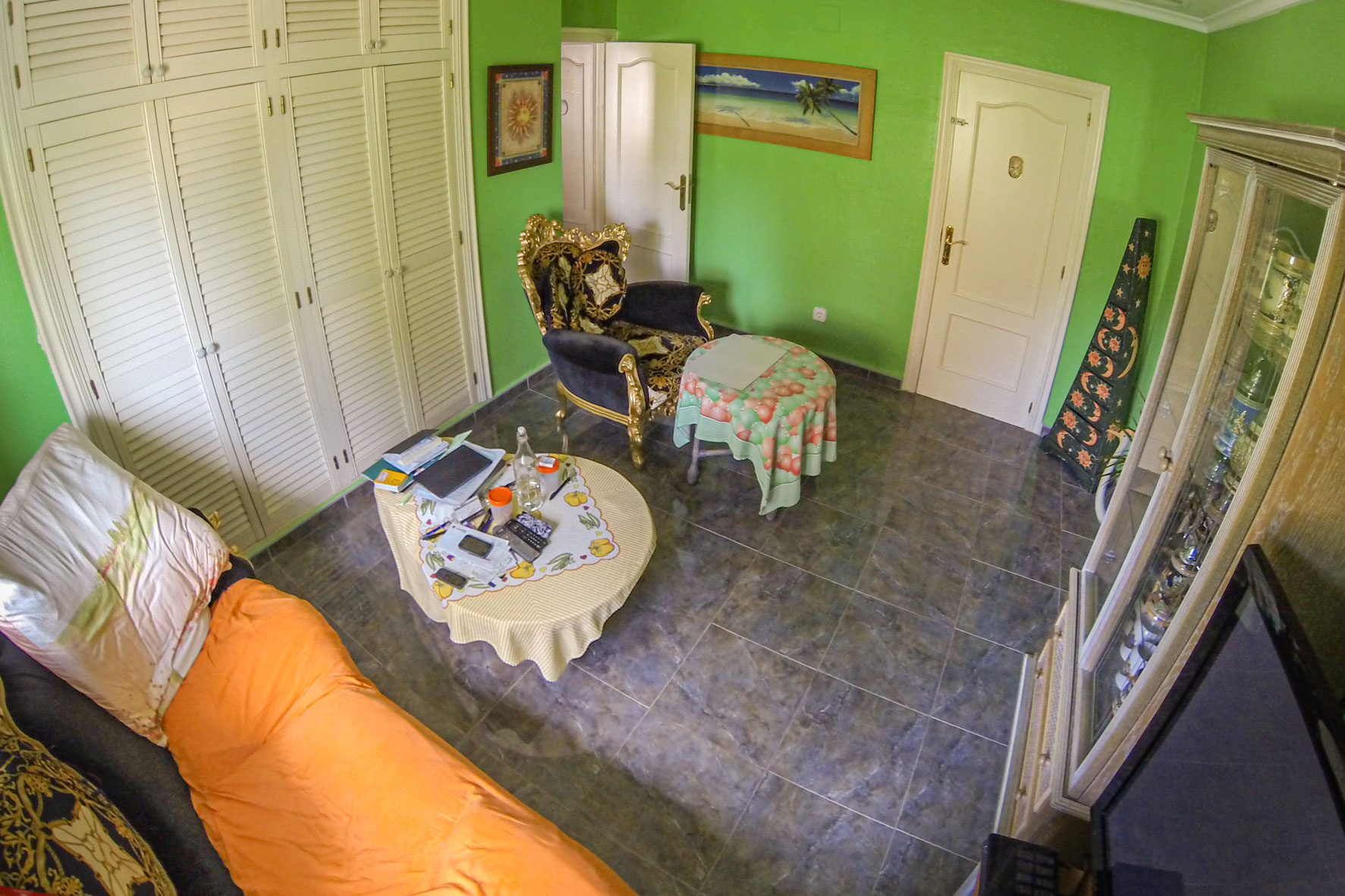 Habitación luminosa con paredes verdes, suelo de baldosas grises y mobiliario variado.