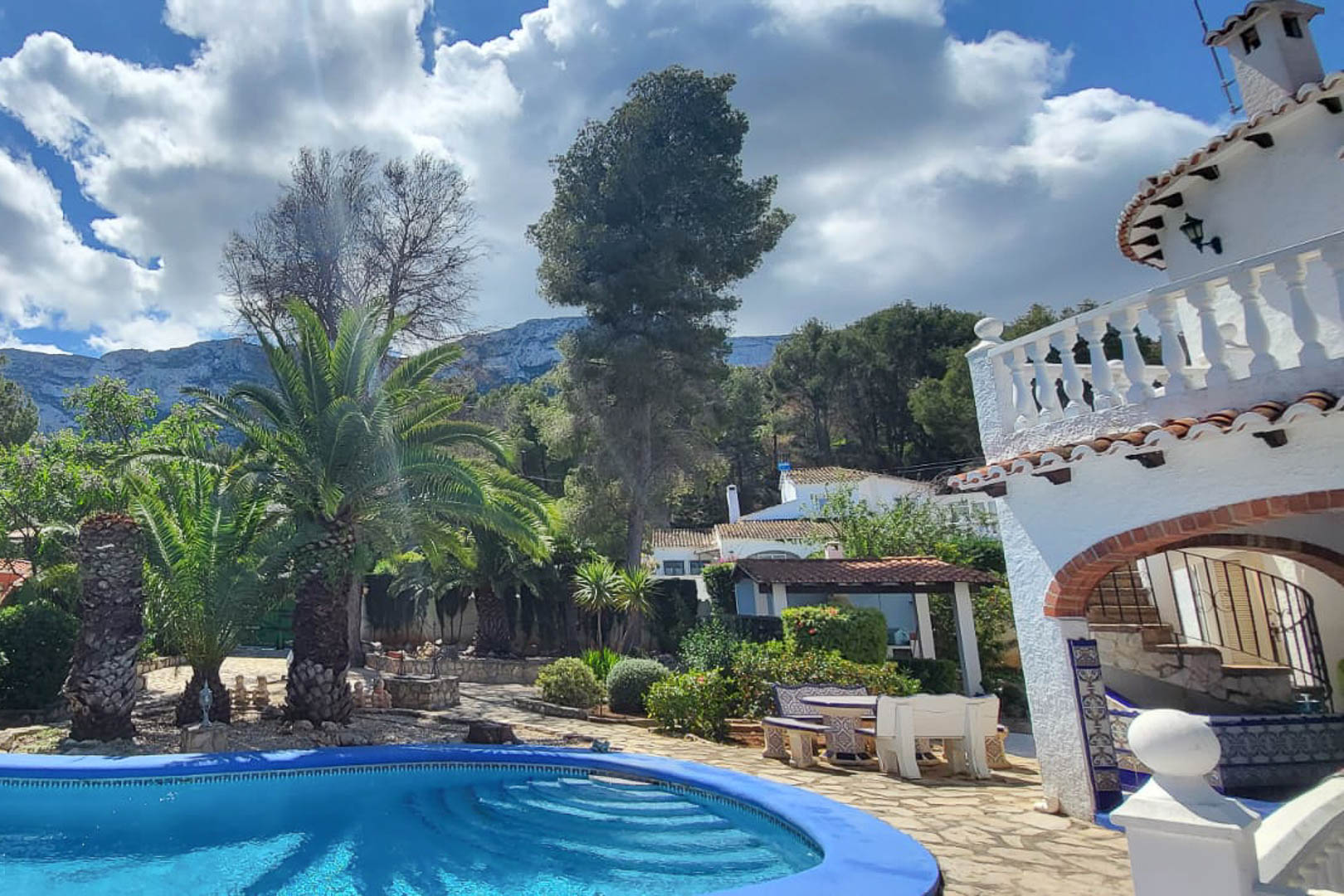 Vista de la piscina azul con acceso escalonado, rodeada de jardines y la casa principal en Denia.
