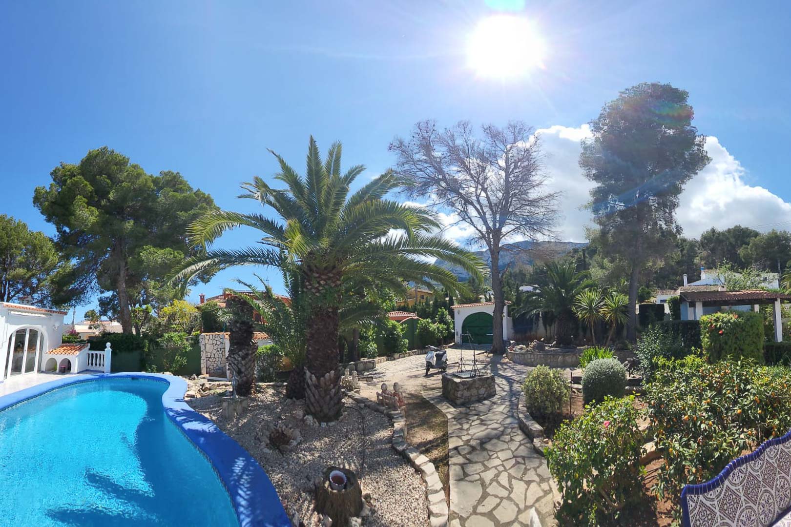 Vista de la piscina azul turquesa y jardines con palmeras y camino de piedra en Denia.