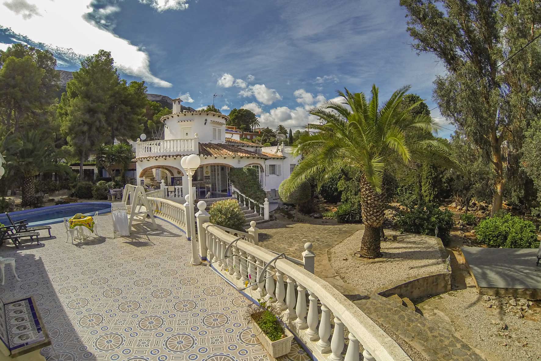 Vista de la terraza con baldosas estampadas, barandilla de balaustres y piscina de la villa.