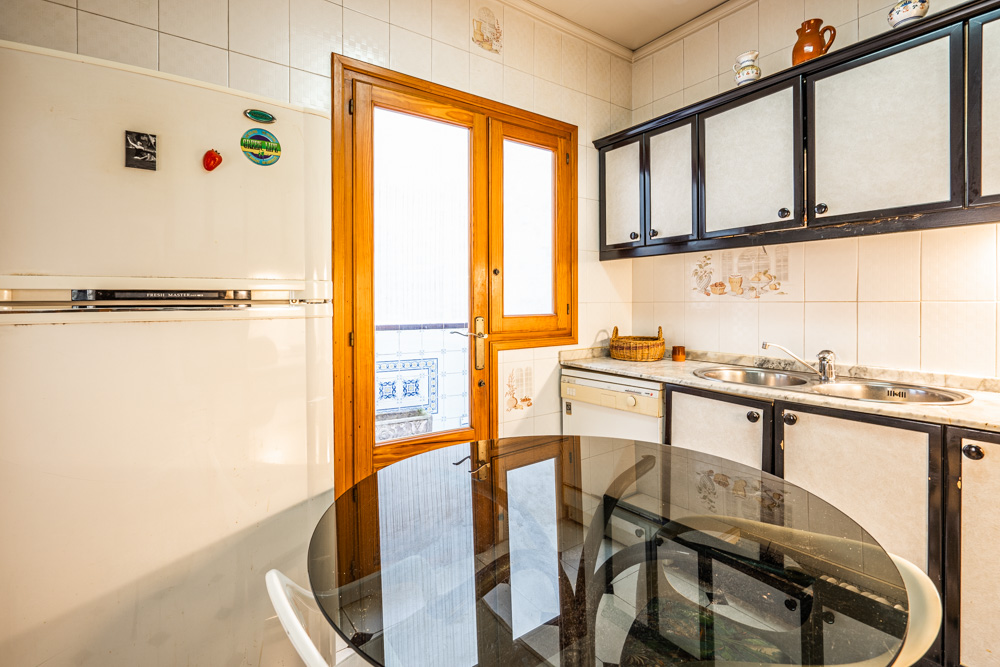 Cocina funcional con armarios de madera oscura, encimera de mármol y acceso directo a un patio interior mediante una puerta acristalada. Incluye mesa de comedor de cristal.