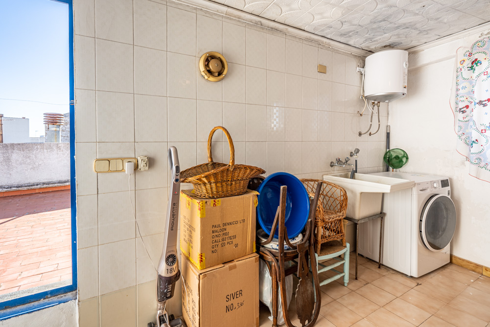 Cuarto de lavandería y trastero con lavadora, termo eléctrico y pila, situado junto al acceso directo a la terraza de la azotea con suelos de baldosa.