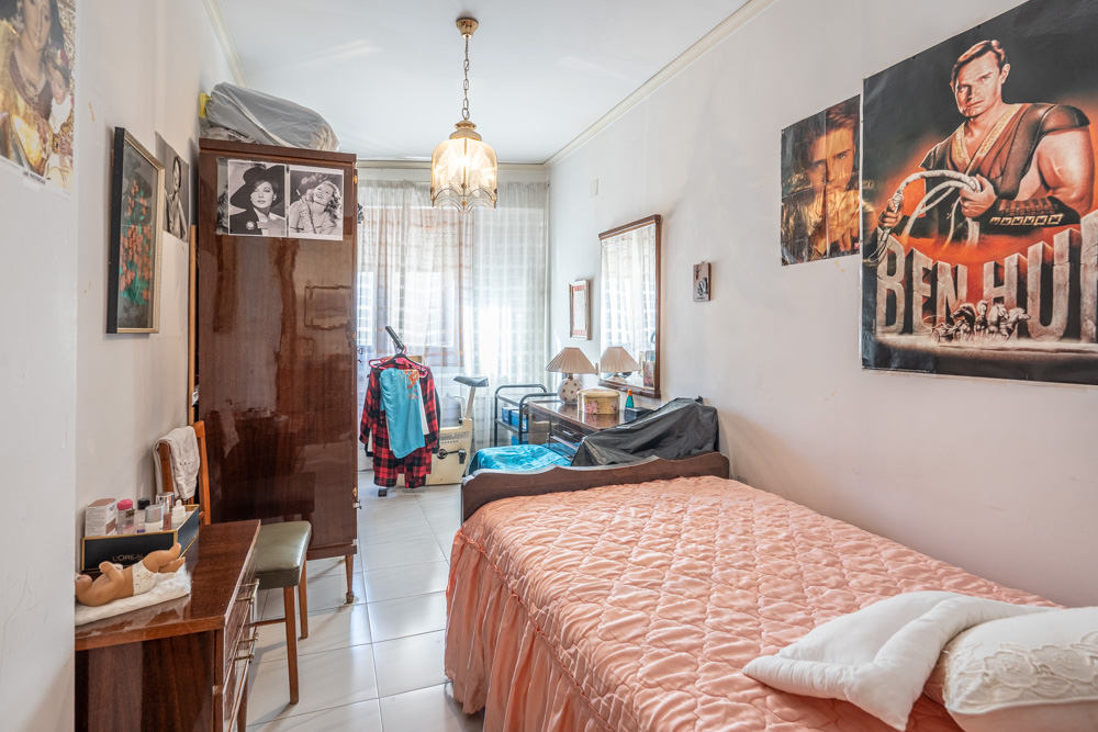 Dormitorio individual con armario de madera oscura, escritorio y suelos de gres. La estancia cuenta con luz natural y una distribución funcional de estilo tradicional.
