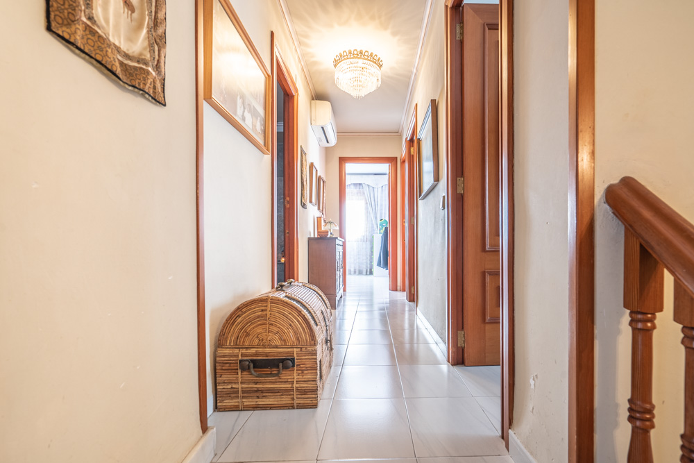 Pasillo de la planta superior con suelos de baldosa clara, puertas de madera maciza y una lámpara de araña clásica. Incluye aire acondicionado y acceso a los dormitorios.