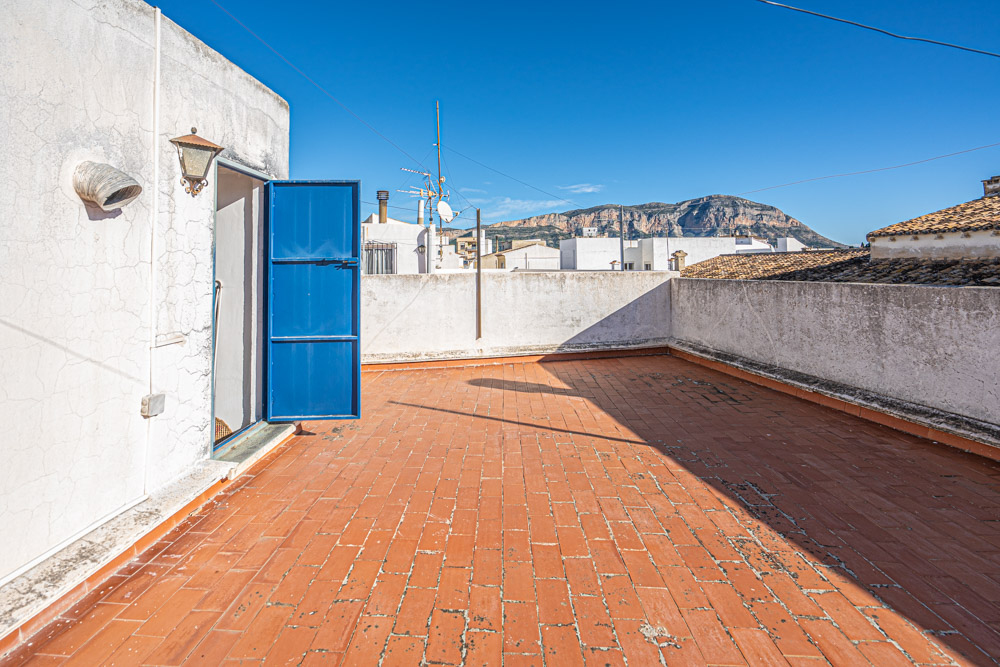 Terraza en la azotea con suelo de baldosas de barro, muros perimetrales blancos y vistas despejadas al macizo del Montgó bajo un cielo despejado.