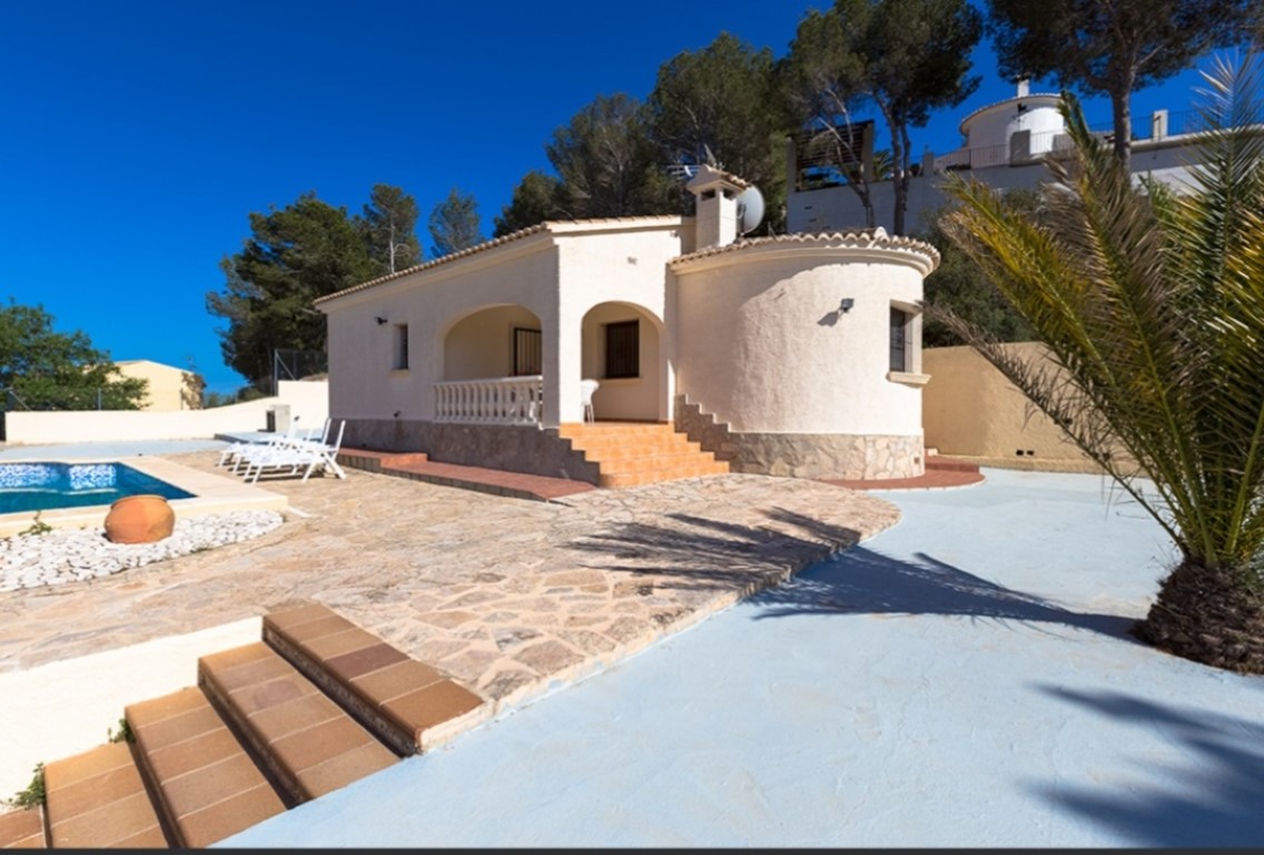 Exterior de villa tradicional con porche arqueado, terraza de piedra natural y piscina privada rodeada de pinos y vegetación mediterránea.
