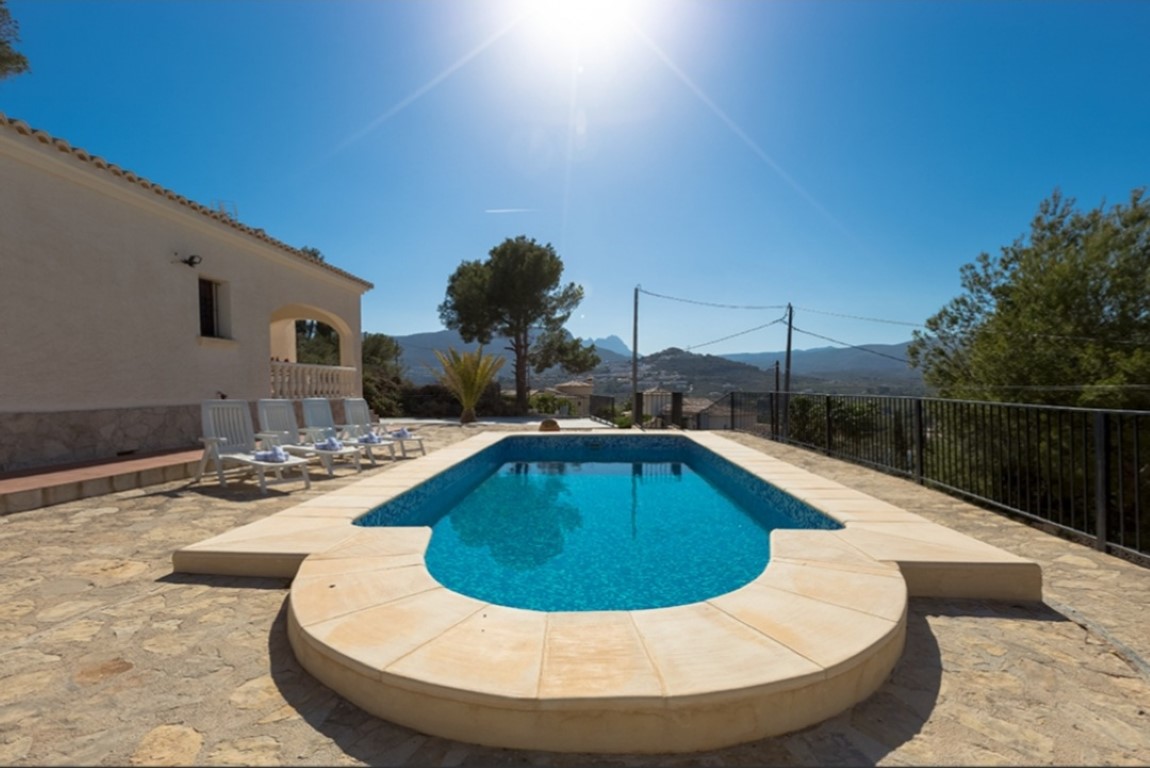 Piscina exterior con terraza de piedra natural y vistas panorámicas a las montañas. Cuenta con tumbonas blancas y una barandilla perimetral metálica negra.