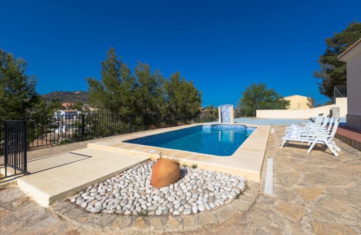 Terraza con pavimento de piedra, piscina rectangular rodeada de tumbonas blancas y vistas panorámicas a las montañas y zonas verdes.