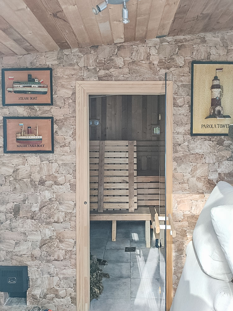 Sauna privada con paredes de piedra natural y puerta de cristal. El interior está revestido íntegramente en madera con bancos multinivel y control de temperatura.
