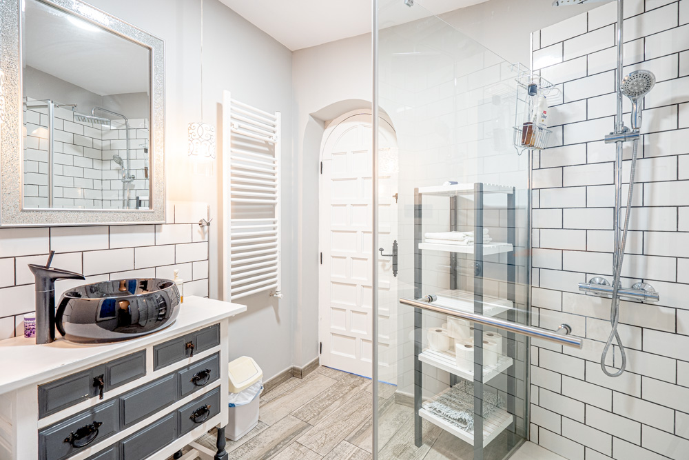 Cuarto de baño reformado con lavabo de porcelana negra sobre mueble rústico, ducha de obra con azulejos tipo metro y mampara de cristal.