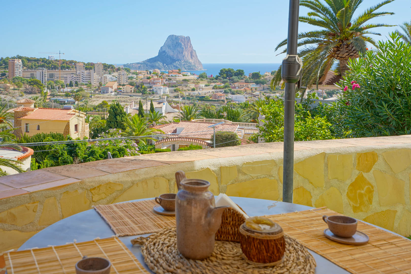 Terraza exterior con zona de comedor y vistas panorámicas al Peñón de Ifach y al mar Mediterráneo, delimitada por muros de piedra natural y vegetación.