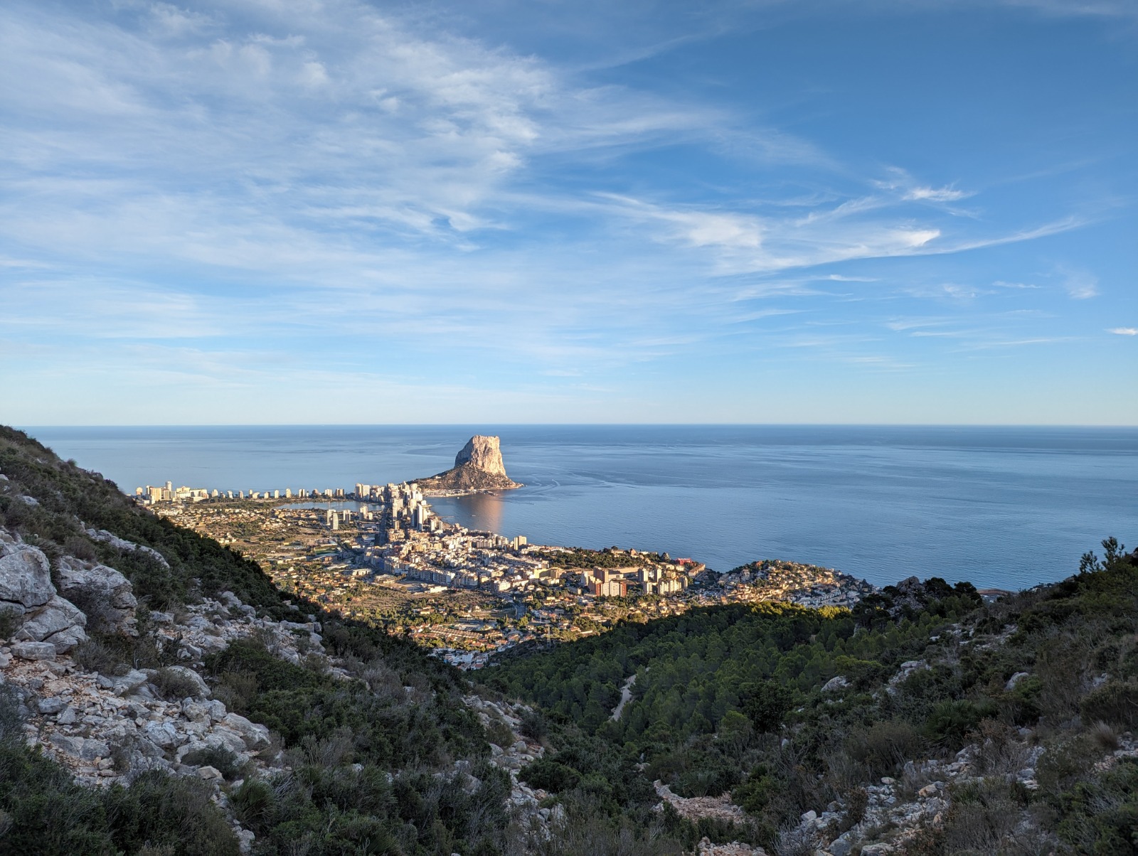 Vista panorámica del Peñón de Ifach y la costa de Calpe desde una posición elevada, destacando el mar Mediterráneo y el entorno montañoso natural.