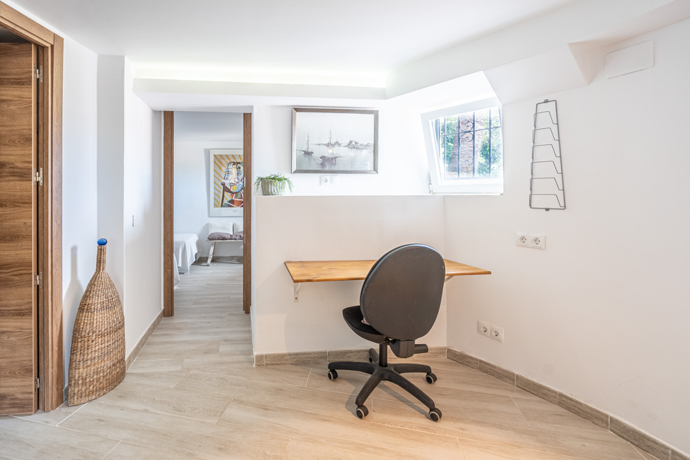 Zona de despacho integrada en el pasillo con escritorio de madera, silla ergonómica e iluminación LED empotrada. Suelos de gres porcelánico y acceso directo a los dormitorios.