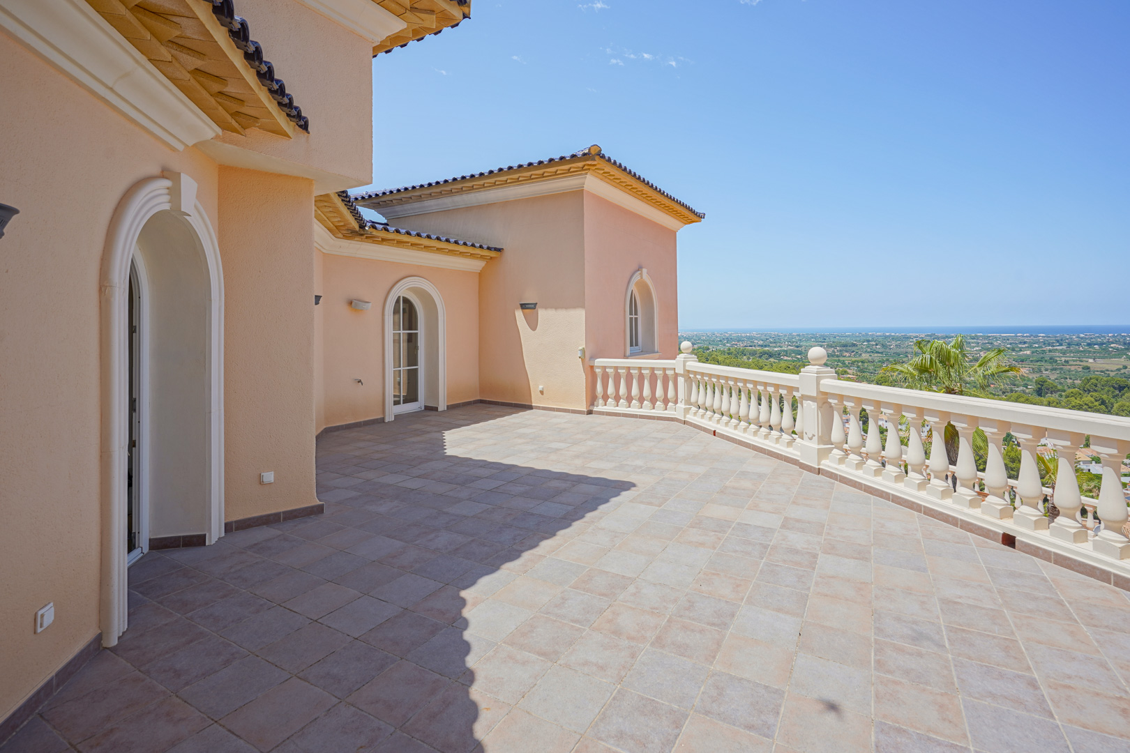 Amplia terraza superior con suelo de gres, balaustrada clásica y vistas panorámicas al valle y al mar Mediterráneo bajo un cielo despejado.