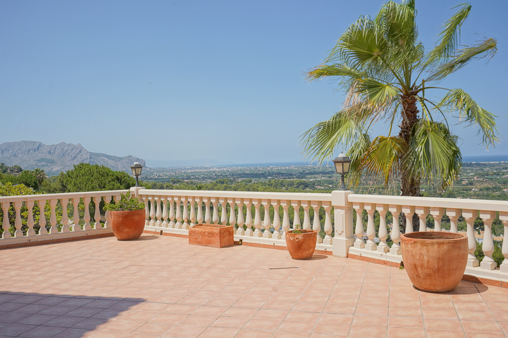 Terraza elevada con suelo cerámico y balaustrada blanca, ofreciendo vistas panorámicas al valle y al mar Mediterráneo bajo un cielo despejado.
