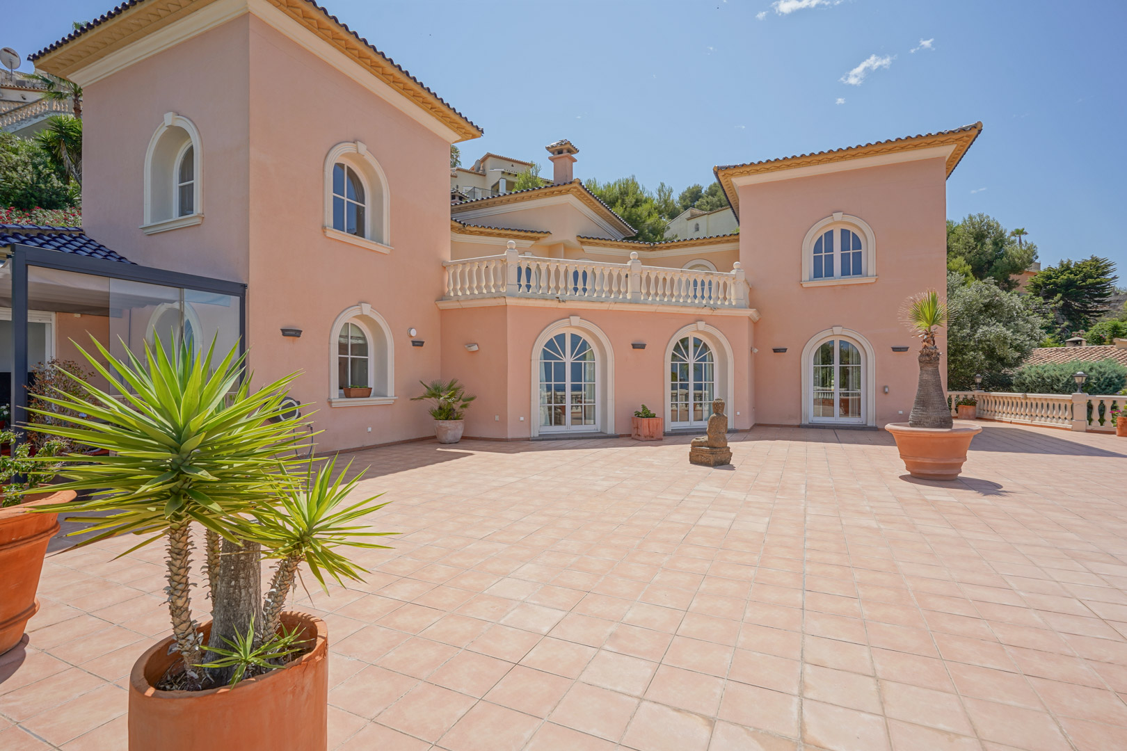 Terraza exterior con pavimentos de terracota, ventanales de arco blanco y fachada en tono salmón con detalles arquitectónicos clásicos.