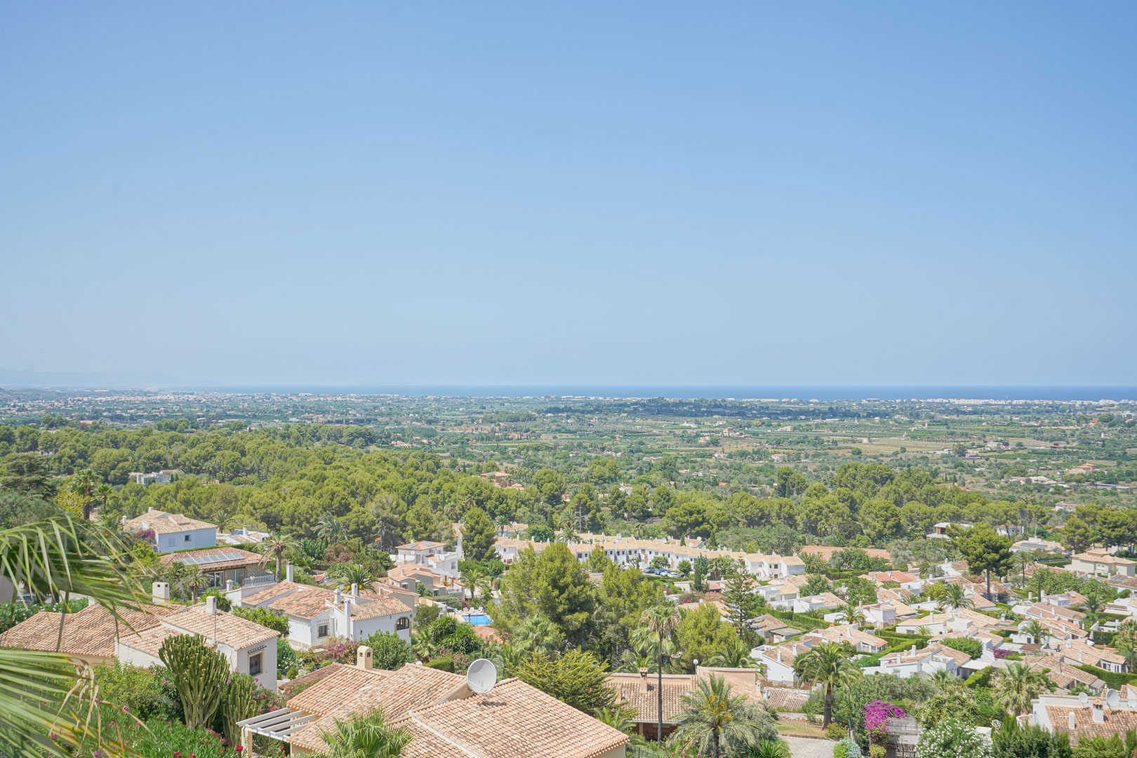 Vista panorámica desde la terraza hacia el valle y el mar Mediterráneo, mostrando la vegetación local y los tejados de terracota de la urbanización La Sella.
