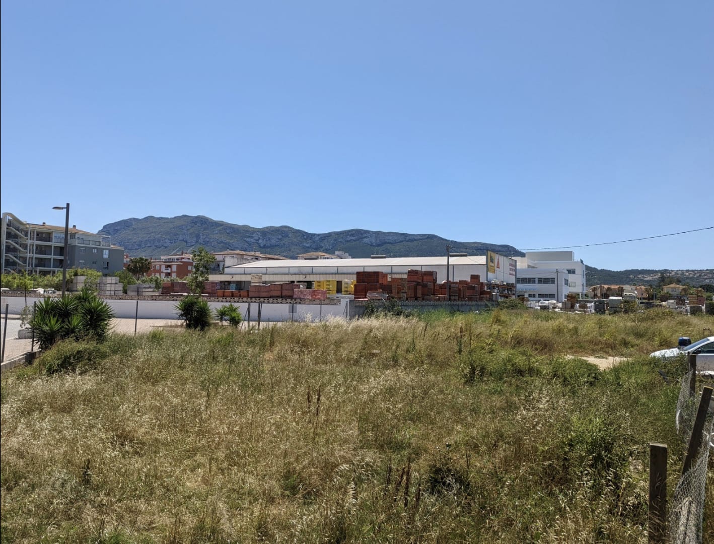 Parcela llana con vegetación natural y vistas despejadas al Montgó, situada junto a zonas comerciales y residenciales consolidadas en Denia.