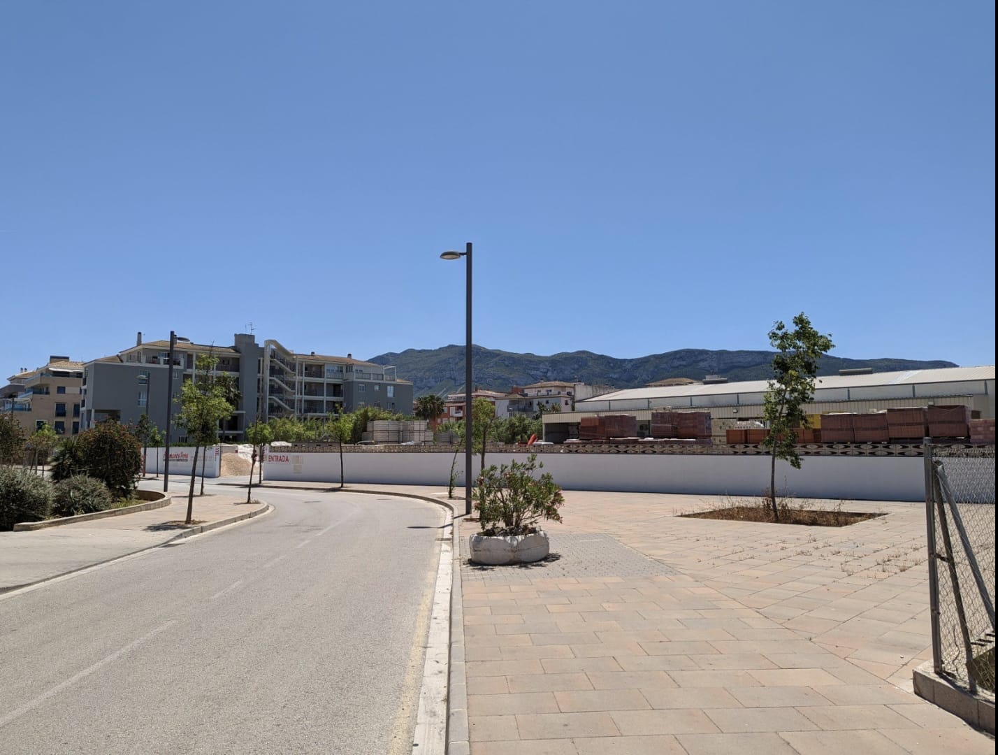 Vista de la parcela urbana con acceso pavimentado y vallado perimetral, destacando las vistas al Montgó y la proximidad a infraestructuras residenciales.