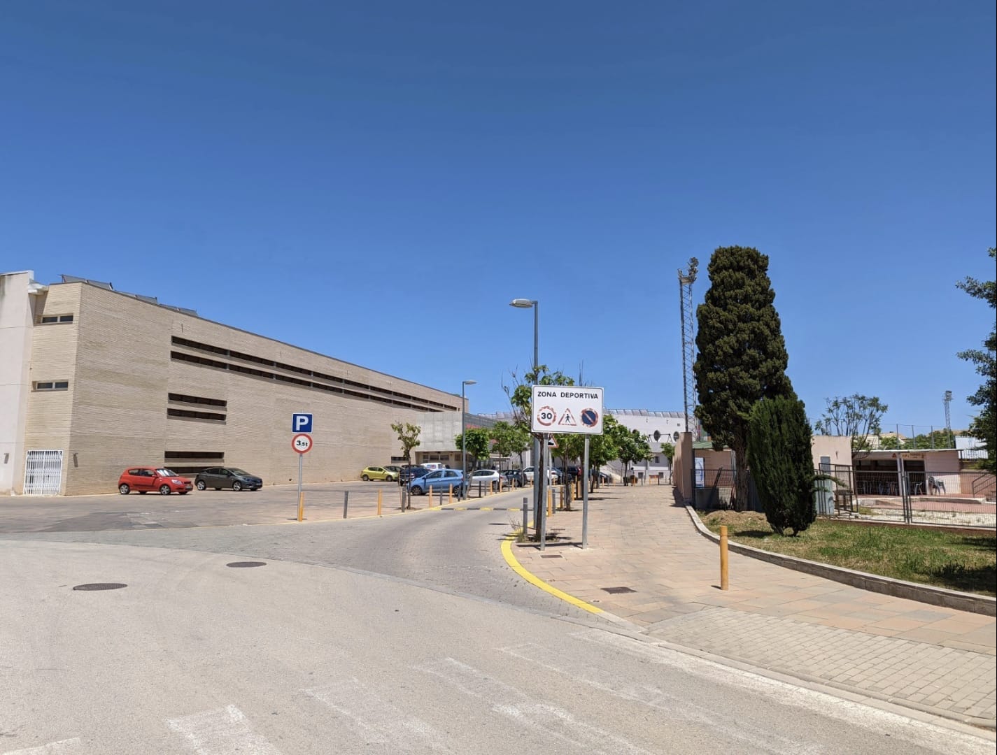 Vista exterior del acceso a la zona deportiva de Denia, situada junto a la parcela, con amplias aceras, señalización vial y edificios institucionales.