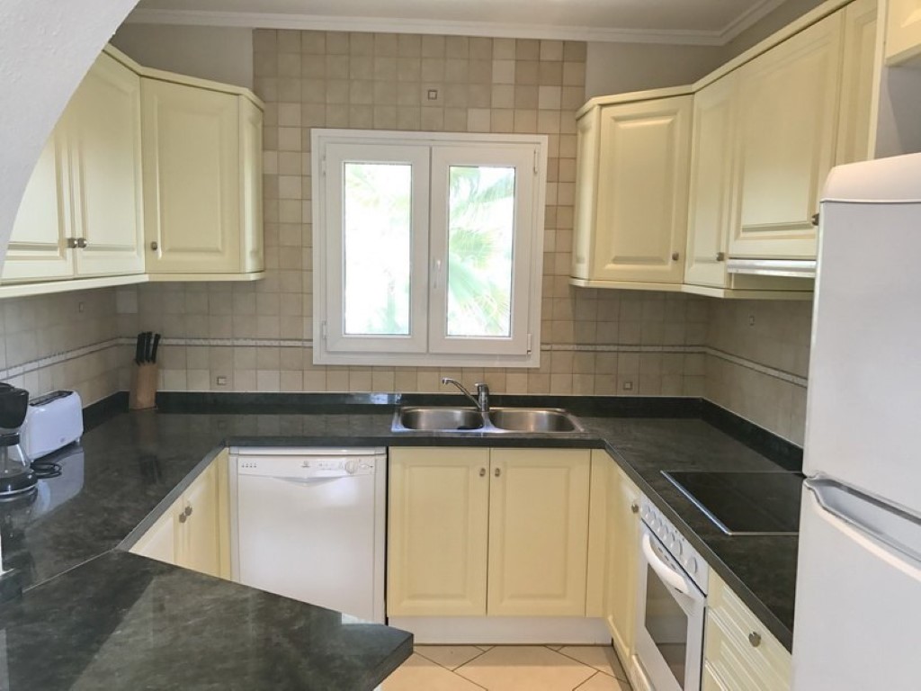 Cocina en forma de U equipada con armarios color crema, encimeras de granito oscuro, fregadero doble de acero y electrodomésticos blancos integrados.