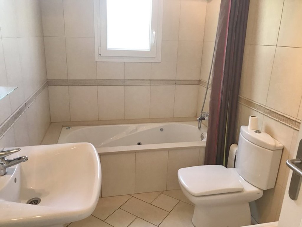 Cuarto de baño con bañera de hidromasaje integrada, lavabo de cerámica blanca e inodoro. Paredes alicatadas en tonos beige con cenefa decorativa y suelo de baldosas claras.