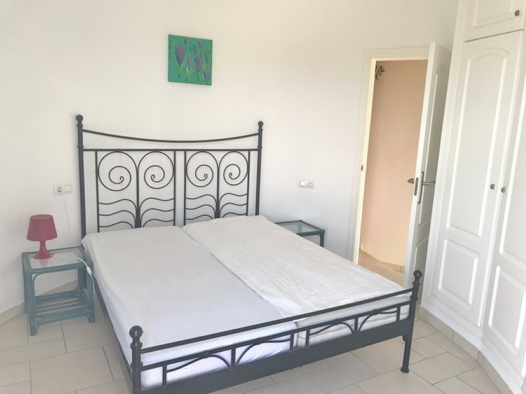 Dormitorio doble con cabecero de forja negra, armarios empotrados blancos y suelos de gres. La puerta abierta muestra el acceso al baño en suite.