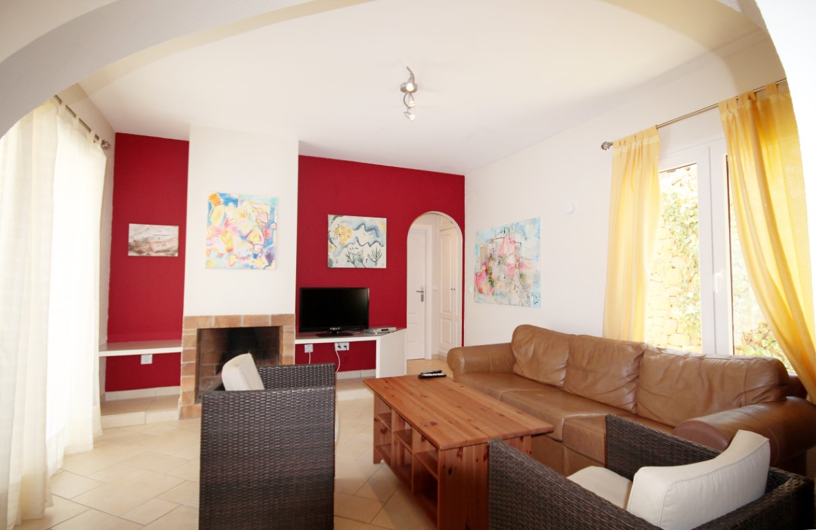 Salón con chimenea de ladrillo, pared de acento roja y sofás de cuero. Cuenta con luz natural, suelos cerámicos y acceso a través de un arco tradicional.