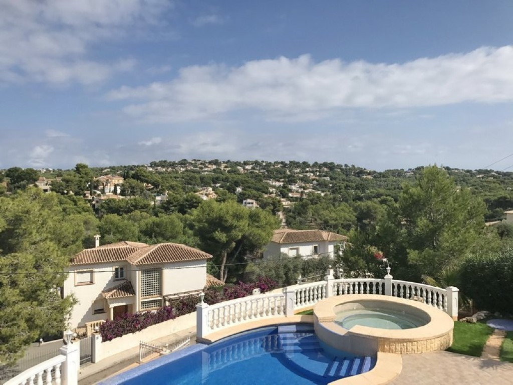 Terraza exterior con piscina de forma curva y jacuzzi circular integrado, con vistas panorámicas al valle boscoso y las villas residenciales de Jávea.