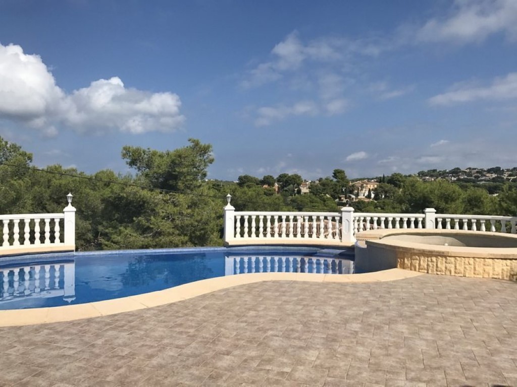 Terraza exterior con piscina de forma curva y jacuzzi integrado, delimitada por una balaustrada blanca con vistas panorámicas al entorno natural de Jávea.