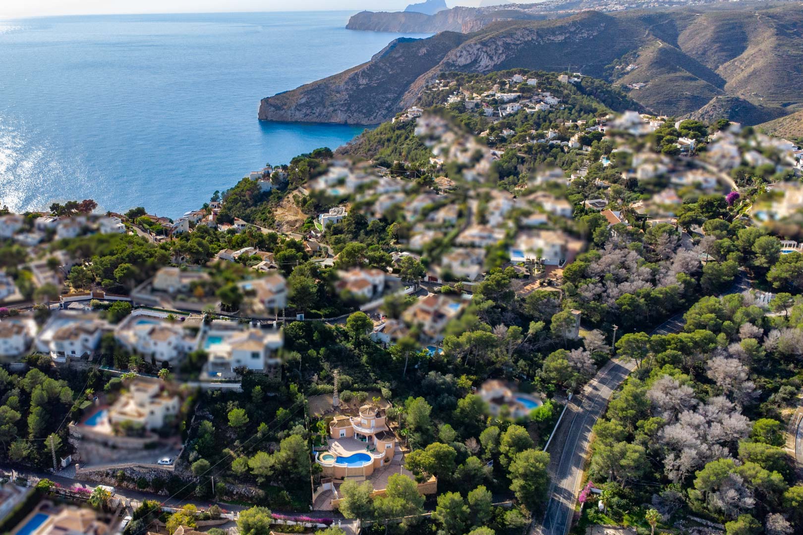 Vista aérea de la villa con piscina curva y zona de jacuzzi, rodeada de vegetación autóctona y con vistas panorámicas al mar Mediterráneo y los acantilados de Jávea.