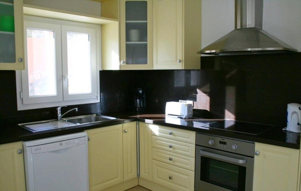 Cocina equipada con armarios en tono crema, encimera de granito oscuro y electrodomésticos integrados. Incluye placa vitrocerámica, horno y fregadero doble bajo la ventana.