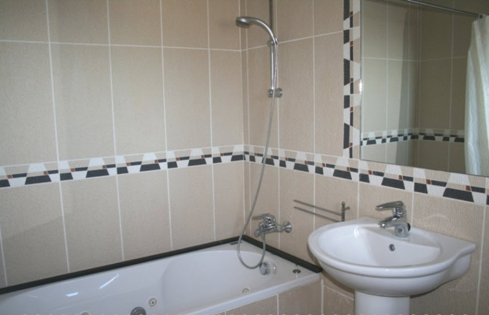 Cuarto de baño con bañera de hidromasaje, lavabo de pedestal y azulejos en tonos beige con cenefa decorativa geométrica y grifería cromada.